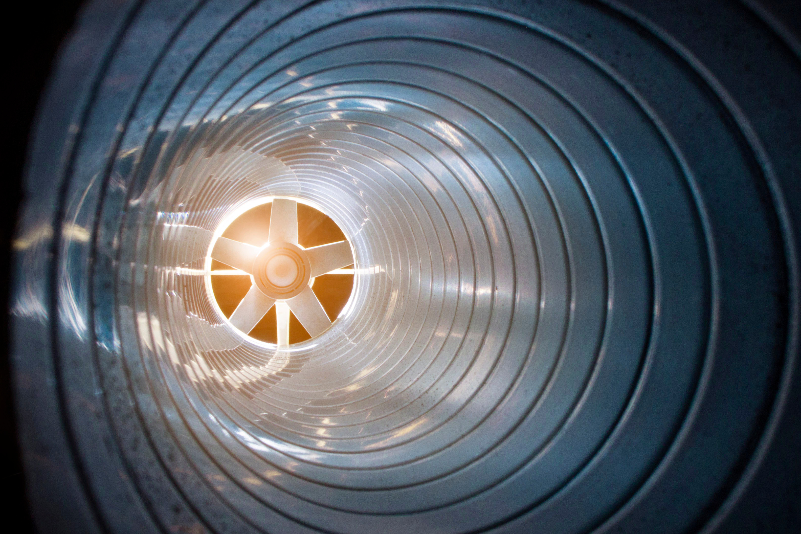 Inside view of an industrial ventilation pipe with a large steel fan at the end.