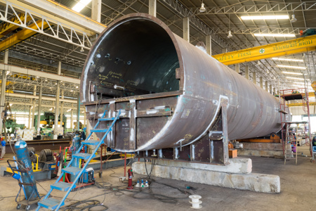 Large, open industrial pressure tank on a factory floor with a blue access ladder.
